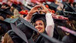 A graduate smiles and holds up their hands in the shape of a heart